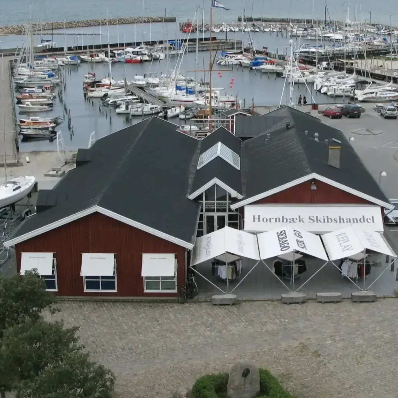 Det røde træhus på Hornbæk Havn set fra oven, med lystbådehavnen i baggrunden